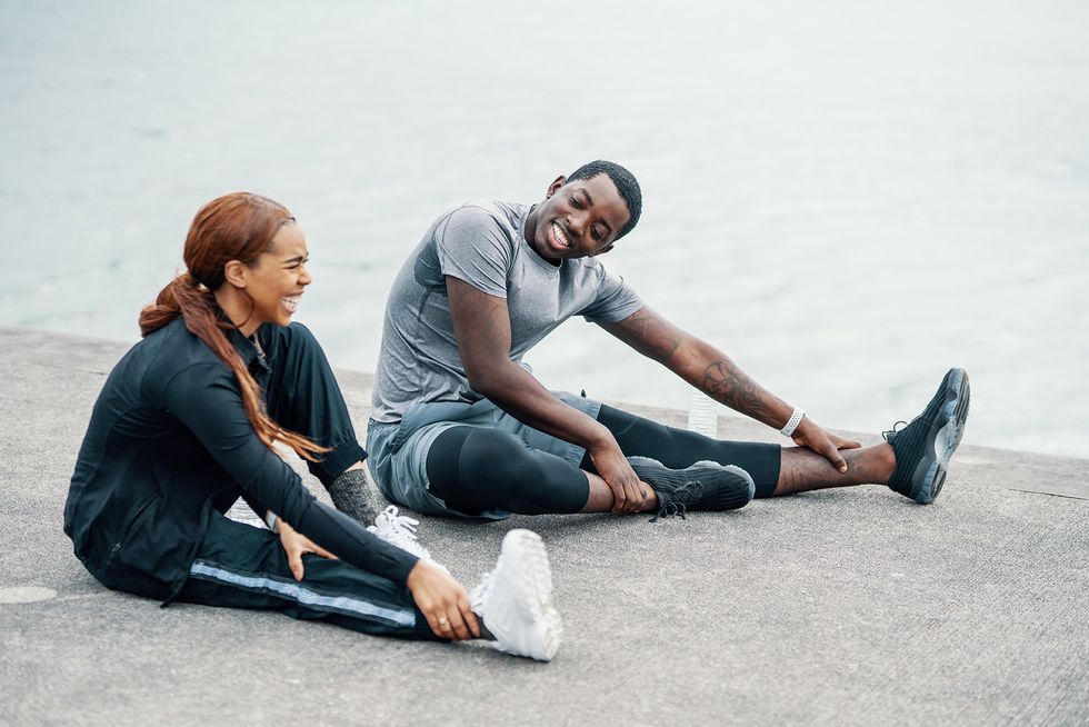 young couple stretching together before or after running or jogging along the coast