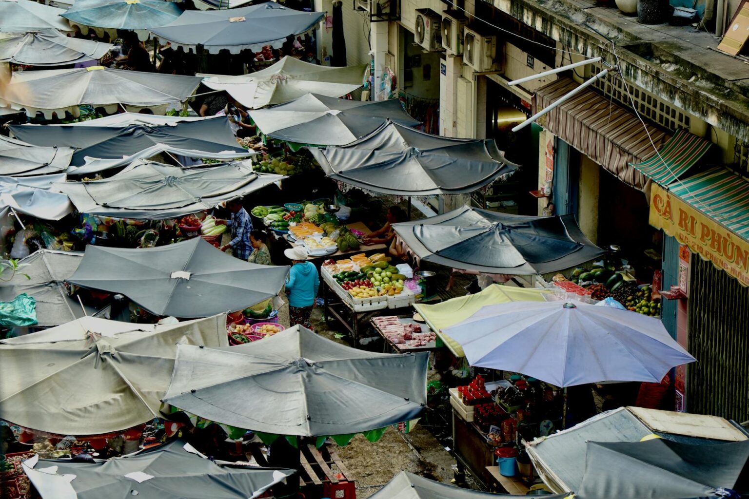 Busy outdoor food market with vendors and shoppers browsing fresh produce stalls
