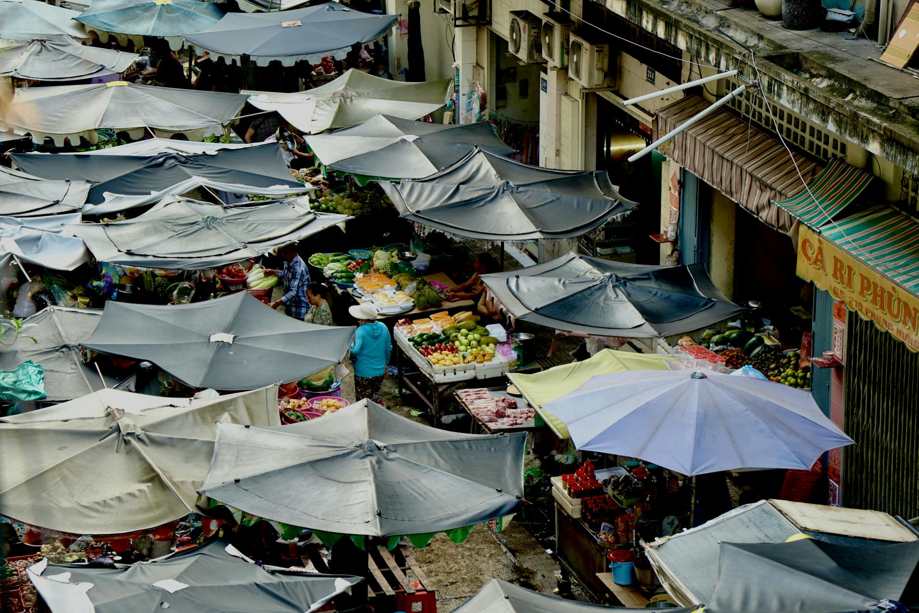 Busy outdoor food market with vendors and shoppers browsing fresh produce stalls