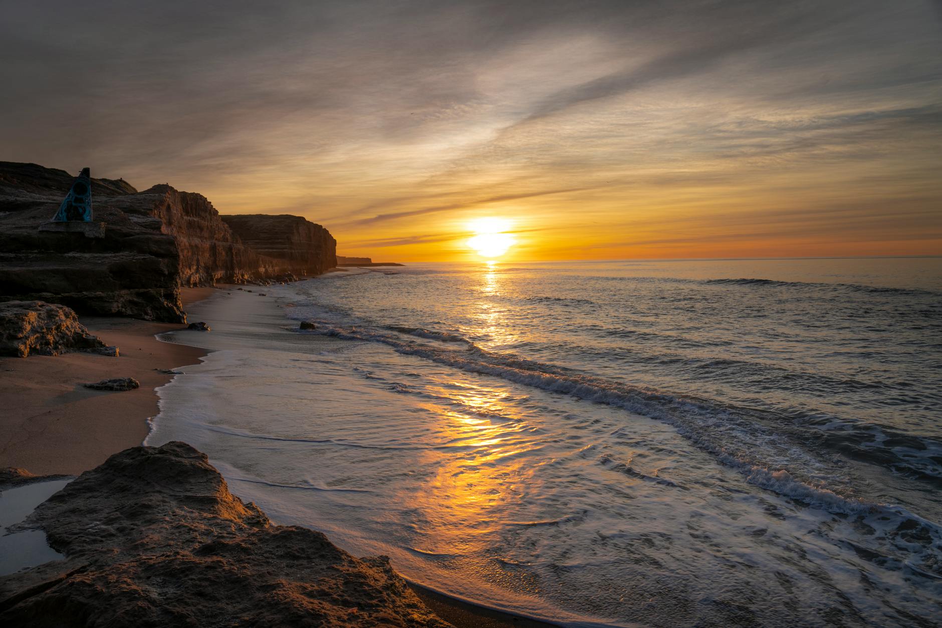 Golden sunrise over ocean beach with early morning light reflecting on sand and waves