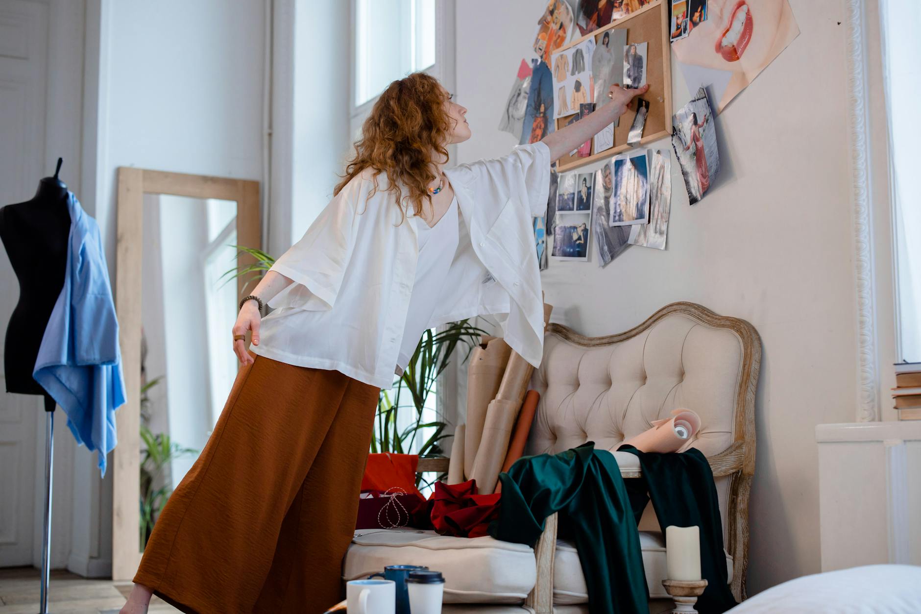 Fashion designer working at studio table with fabric samples and design sketches spread across workspace