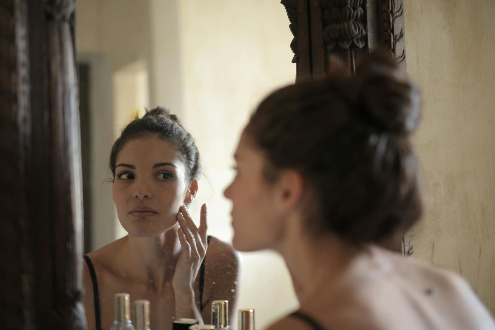 Person looking in mirror while doing skincare routine incorporating face yoga exercises