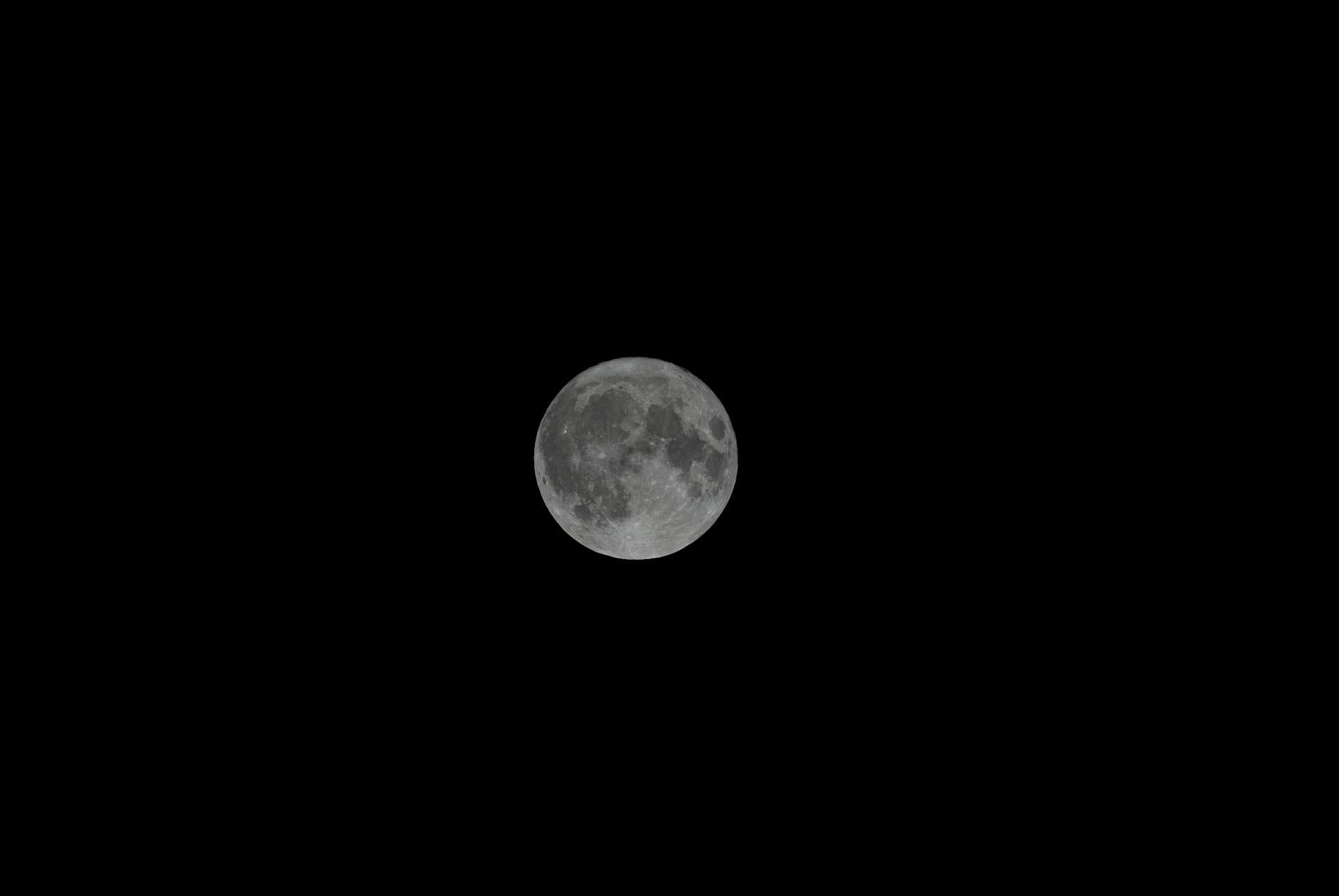Bright full moon illuminating dark evening sky with scattered clouds
