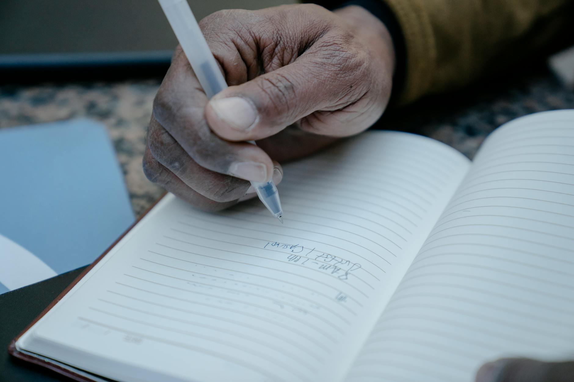 Person's hands writing in journal with pen on wooden desk surface