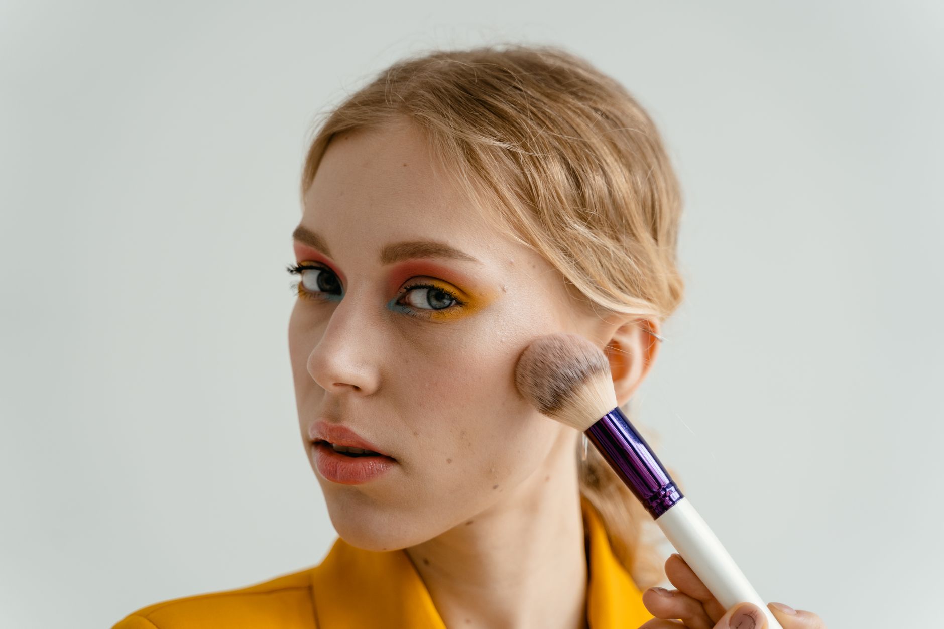 Woman blending blush on cheekbones with a soft brush in natural light