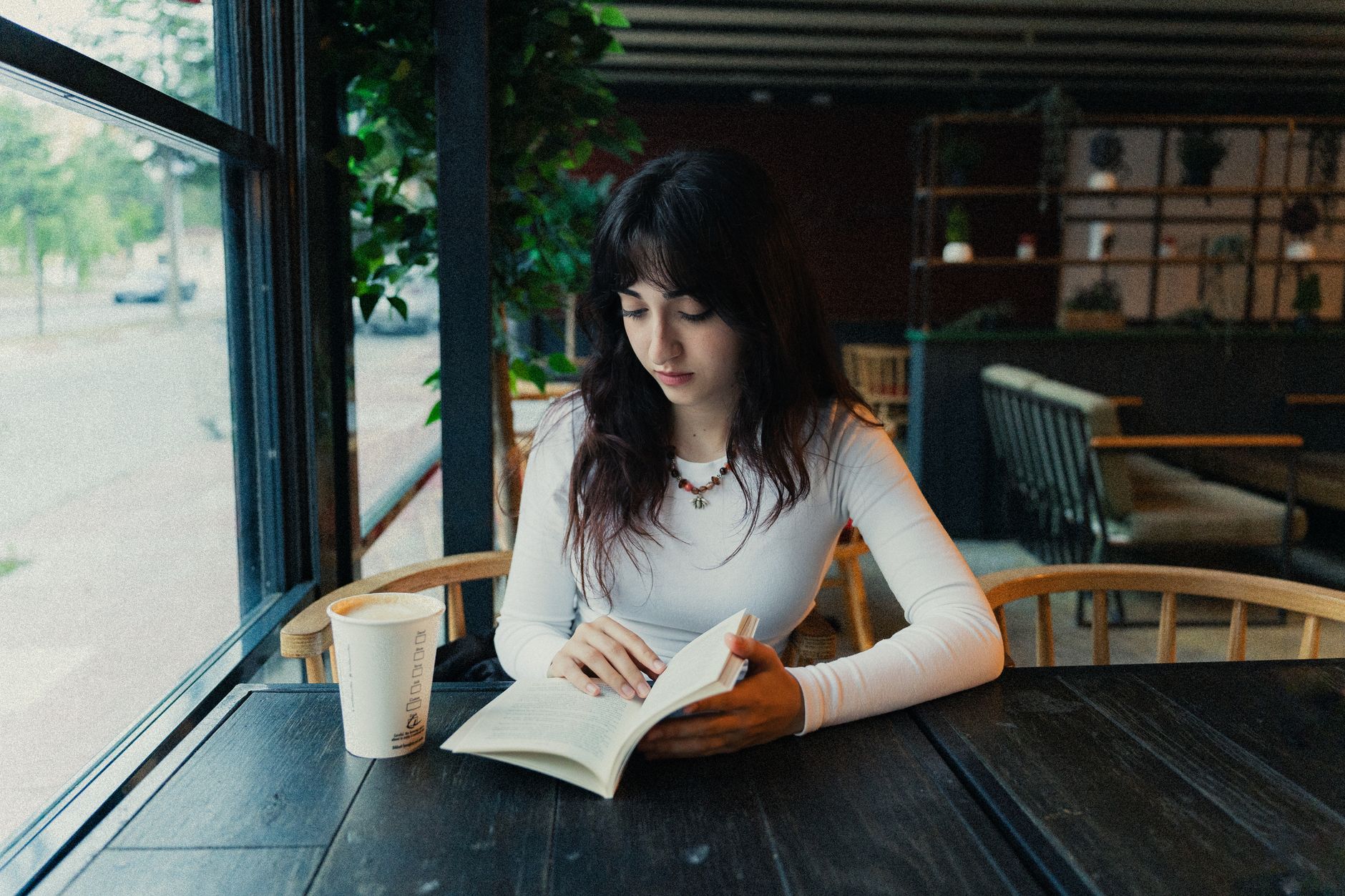 Young woman reading a book alone at a coffee shop table