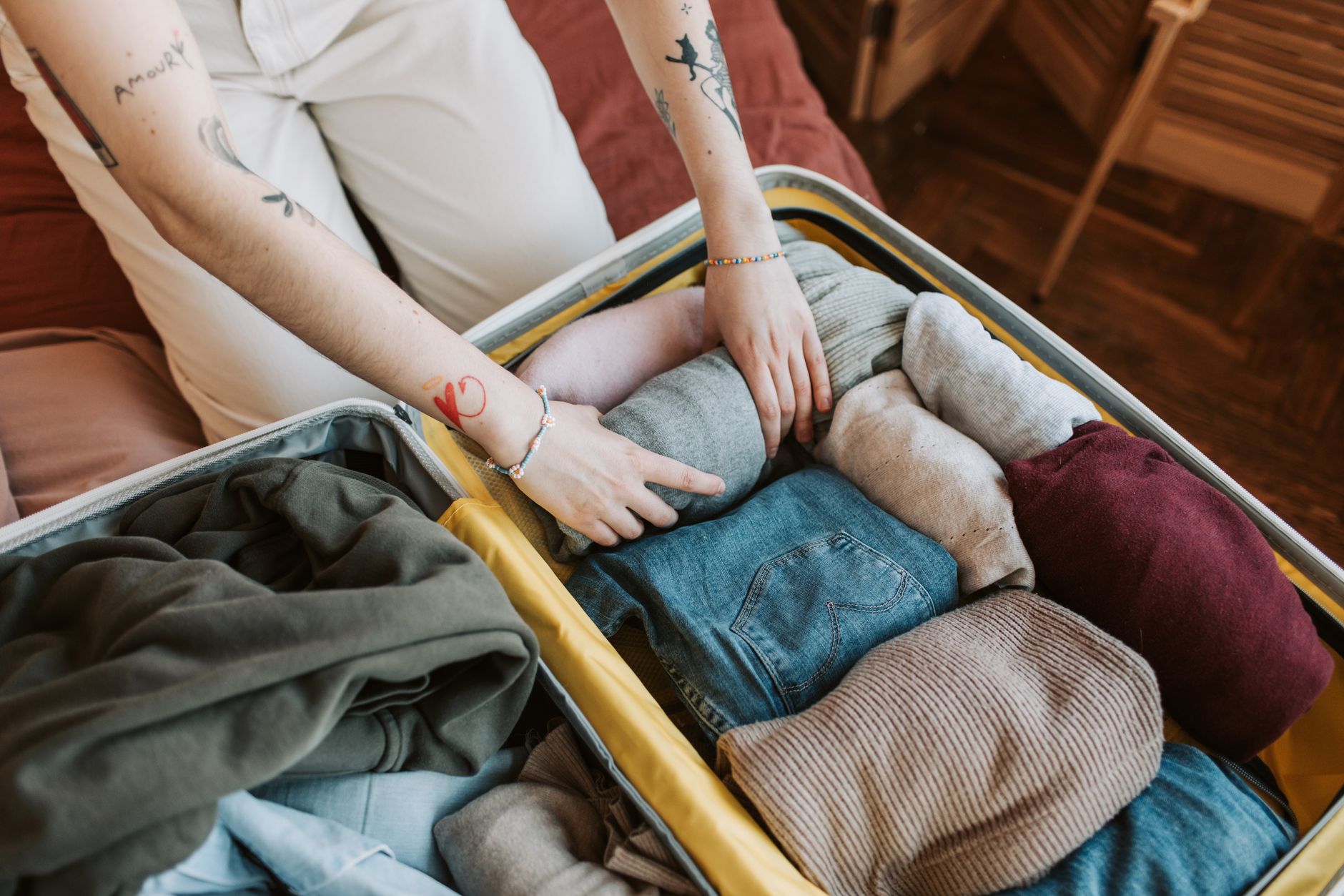 Neatly folded linen travel clothes and skincare essentials on a bed