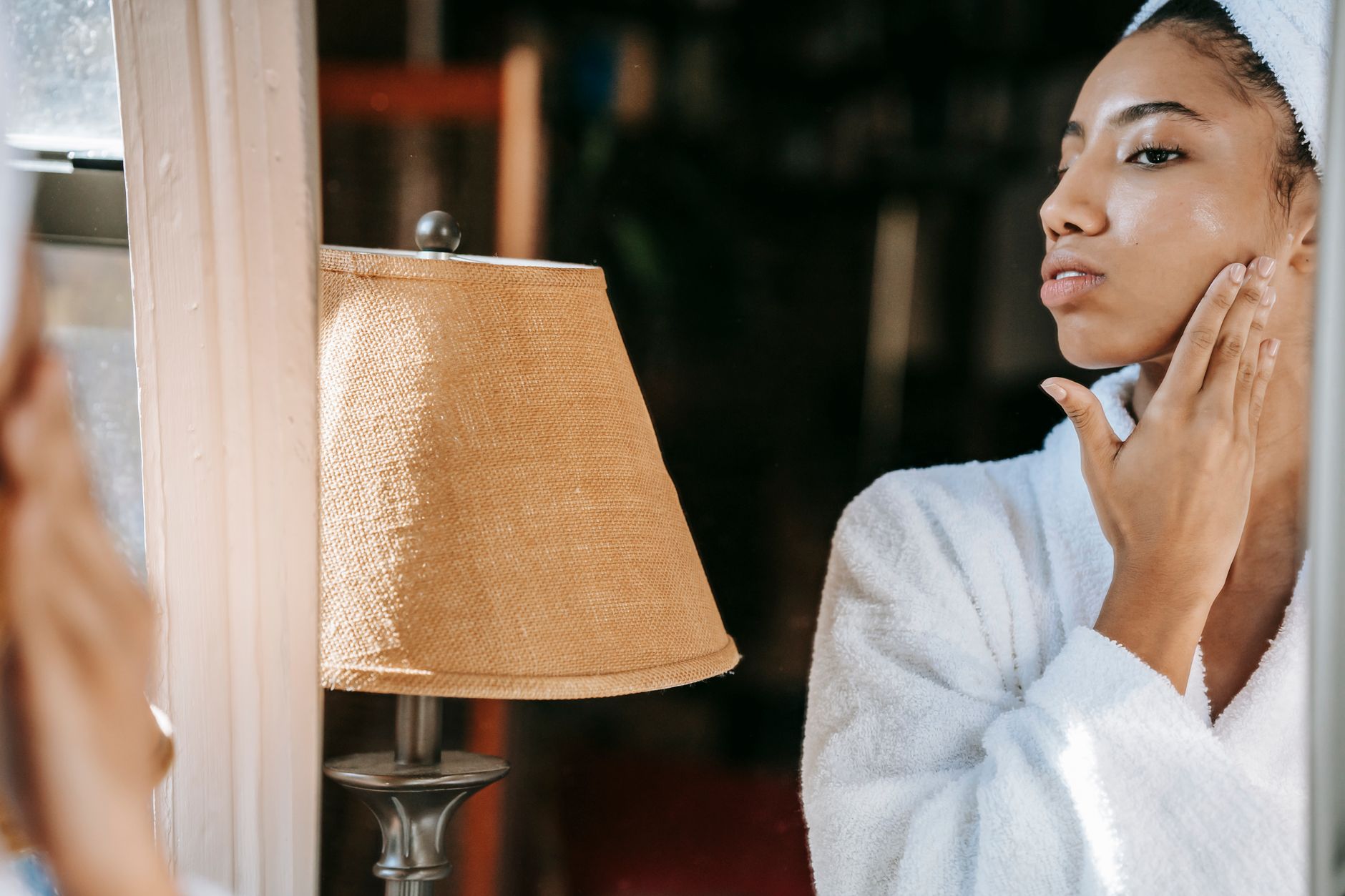 Woman applying skincare product in mirror, focused self-care moment
