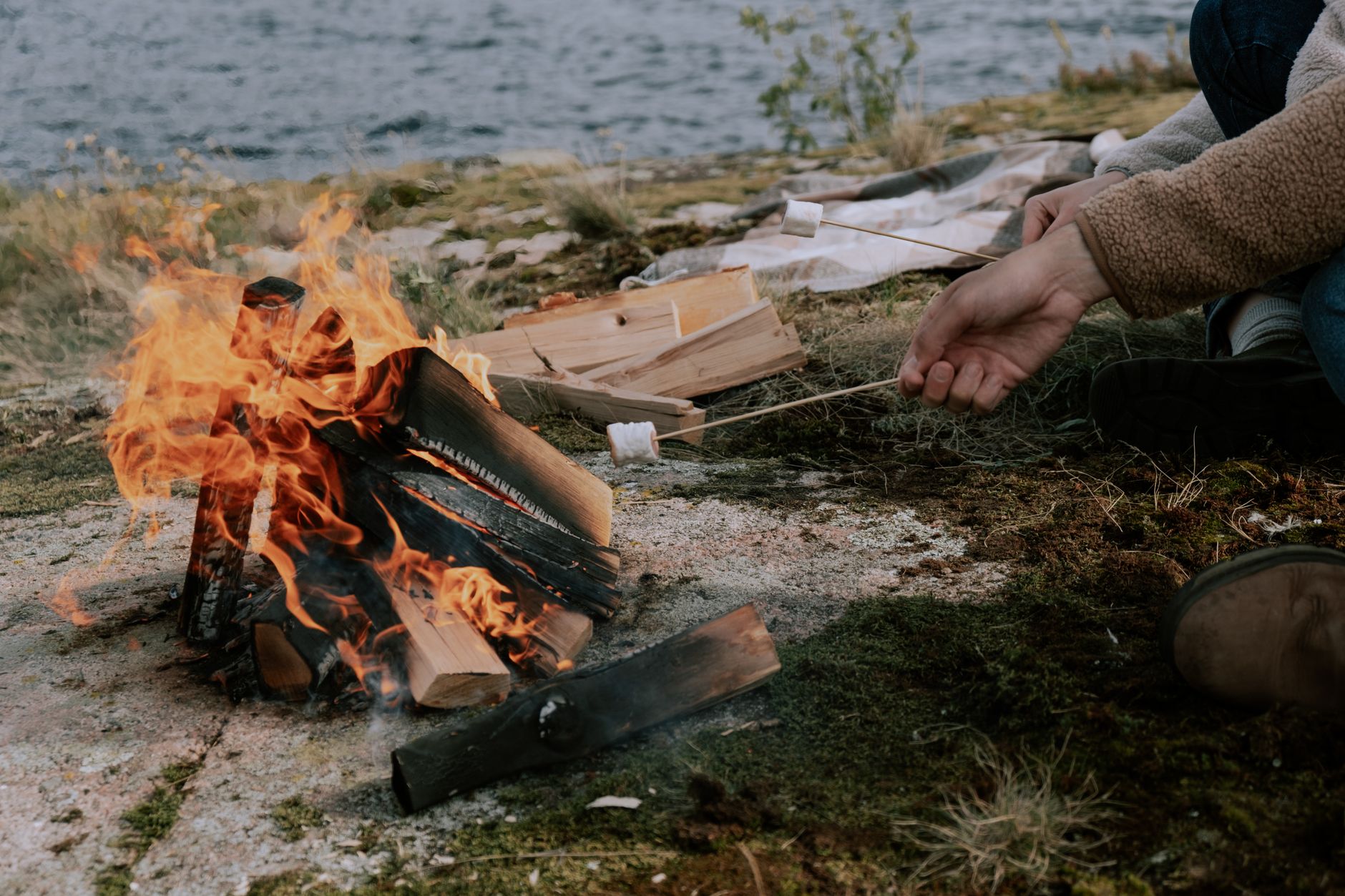 People toasting marshmallows around a glowing campfire at dusk